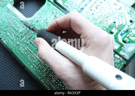 A right hand holding a soldering iron and soldering a through hole component on its track on a green printed circuit board, on black background Stock Photo