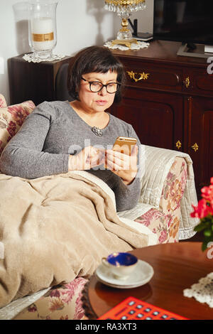 attractive elderly woman lying on the couch and surfing the internet at home. Stock Photo