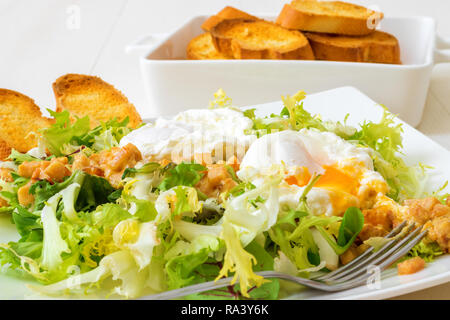 Classic French salad, great salad Lyonnaise. Dish with green leaves of lettuce, Dijon mustard sauce with pieces of fried bacon, grilled French bread,  Stock Photo
