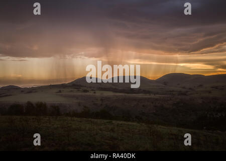 Rain falling on a distant mountain with orange sunset Stock Photo