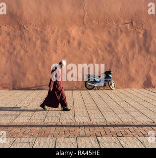 Man walks along red-orange city walls of Marrakech, Morocco