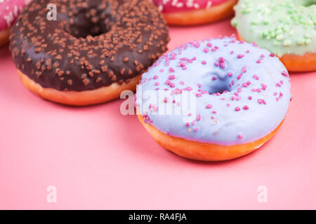 Sweet colorful tasty donuts with icing and sprinkles on pastel pink background.