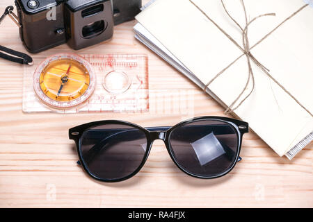 Sunglasses, old film camera, compass and a bunch of letters on light wooden background. Concept of summer travels. Stock Photo