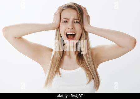Girl panicking screaming, losing temper holding hands on head from overthinking, looking worried and depressed standing over gray background, yelling concerned and desperate Stock Photo