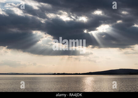 Beautiful sunset on a lake, with sunrays coming down under an overcast sky Stock Photo
