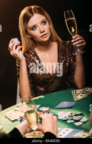 attractive girl holding glass of champagne and poker chip at table in casino Stock Photo