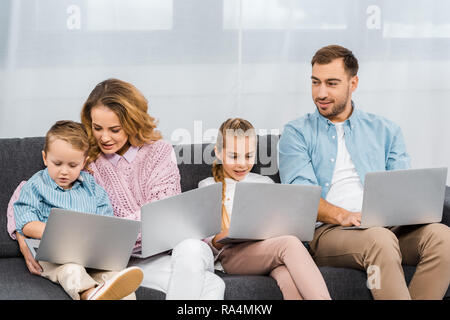 happy family sitting on sofa and using laptops in apartment Stock Photo