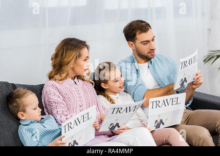 happy family sitting on sofa and reading travel newspapers in apartment Stock Photo