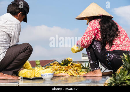A Vietnamese man and woman prepare pineapple fruit to sell in floating market on Hau River. Can Tho, Mekong Delta, Vietnam, Asia Stock Photo