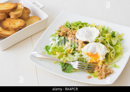 Classic French salad, great salad Lyonnaise. Dish with green leaves of lettuce, Dijon mustard sauce with pieces of fried bacon, grilled French bread,  Stock Photo