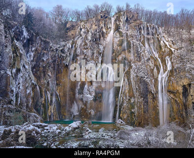 Frozen big waterfall, covered in snow and ice falling into green pool of water.  View from top to bottom of horseshoe cliffs . Scene in Plitvice Natio Stock Photo