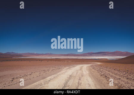 Dirt road through the salt flats of Siloli, Bolivia winding through an arid desert landscape with distant mountains Stock Photo