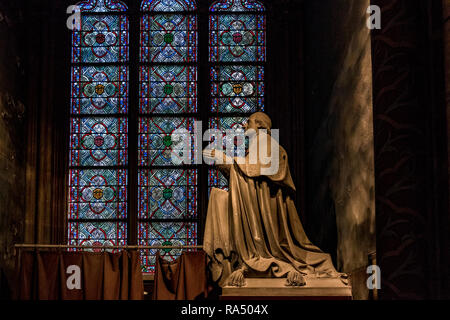A statue of Archbishop Sibour stands in front of a stunning blue and green stained glass window at Notre-Dame Cathedral , Paris Stock Photo