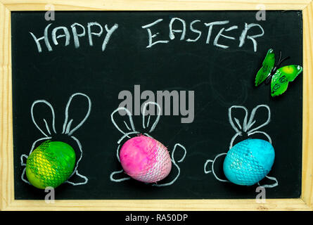 three colorful, pastel Easter eggs with painted rabbit ears against the background of a blackboard Stock Photo