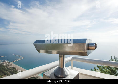 Metal coin operated telescope isolated at beautiful summer panoramic view at cityscape, blue sky and sea water. Turkey, Antalya city. Stock Photo