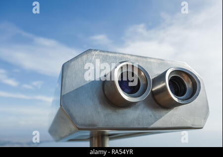 Closeup view of coin operated binocular viewer for looking in details at beautiful summer landscape. Isolated at blue sky background. Horizontal photo Stock Photo