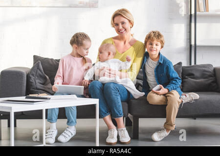 happy mother smiling at camera while sitting on couch with three adorable children Stock Photo