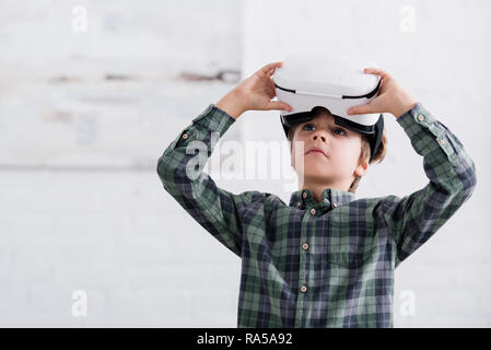 adorable boy using virtual reality headset and looking away at home Stock Photo