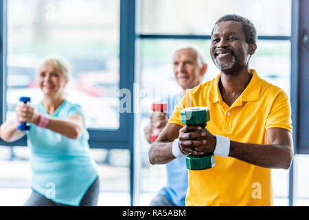 african american sportsman and his friends exercising with dumbbells at gym Stock Photo