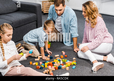 parents and siblings playing with wooden blocks on floor in living room Stock Photo