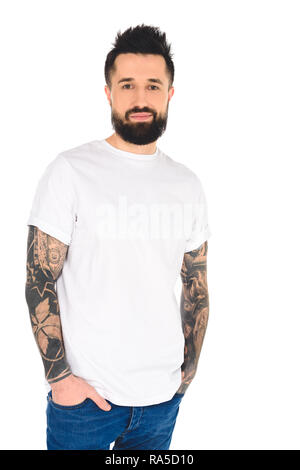 handsome bearded man with tattoos and hands in pockets looking at camera isolated on white Stock Photo