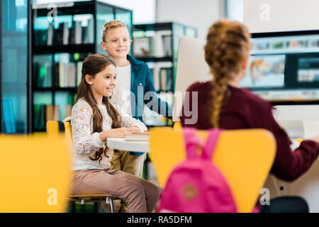 cute smiling schoolkids studying with desktop computers in library Stock Photo