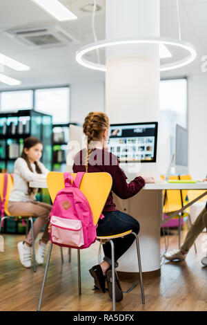 focused schoolgirls sitting and using desktop computers in library Stock Photo
