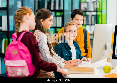 boy smiling at camera while using computer with classmates in library Stock Photo