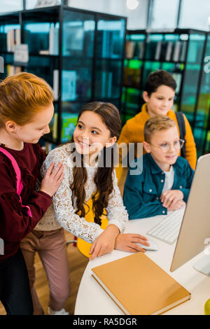 beautiful happy schoolchildren using desktop computer together in library Stock Photo