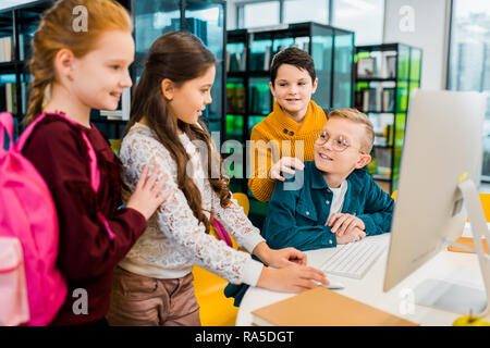cute smiling schoolchildren using desktop computer together in library Stock Photo