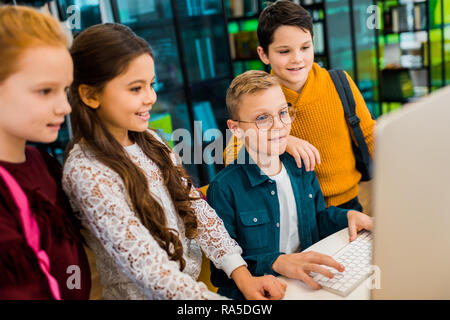 cute happy schoolkids using desktop computer in library Stock Photo