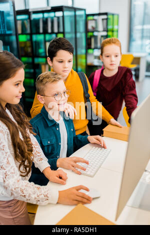 high angle view of adorable smiling schoolkids using desktop computer in library Stock Photo
