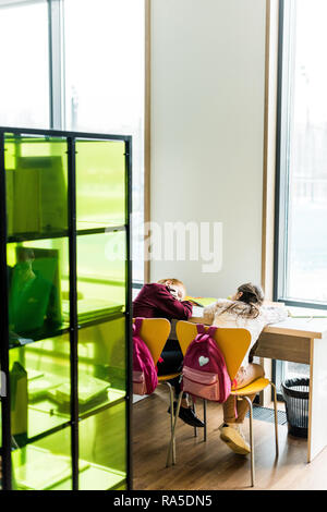 back view of bored schoolgirls sleeping on desk in library Stock Photo