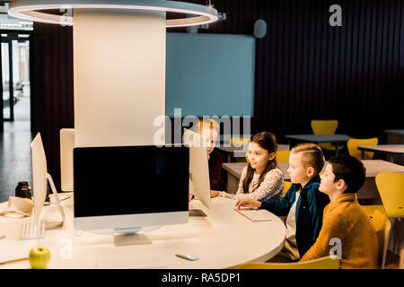 adorable schoolchildren sitting and using desktop computer together in modern library Stock Photo