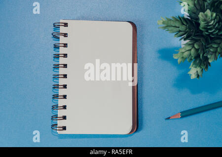 Blank notebook, pencil and tree in pots on a blue background Stock Photo