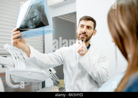 Handsome dentist checking panoramic x-ray of a jaw during the medical consultation with woman patient in the dental office
