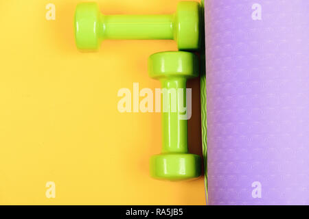 Barbells in small size on yoga mat, close up. Healthy shape and sport concept. Dumbbells made of light green plastic on yellow and purple background, top view. Shaping and fitness equipment Stock Photo
