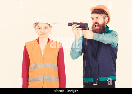 Annoying repair concept. Man with drill drills head of woman, white background. Husband annoyed wife. Woman with bored face in helmet, hard hat. Builder, repairman makes hole in female head. Stock Photo