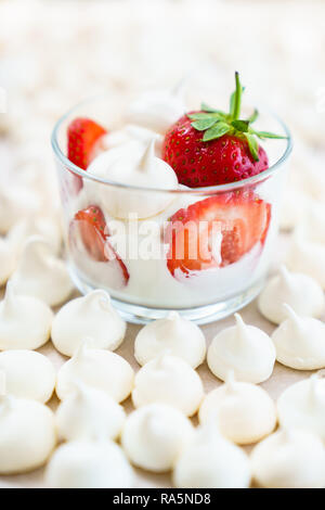 Whipped cream, meringues and fresh strawberries in a glass bowl surrounded by mini meringues. High resolution Stock Photo