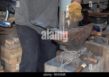 The blacksmith drives a hole into red hot metal on top of the anvil. Stock Photo