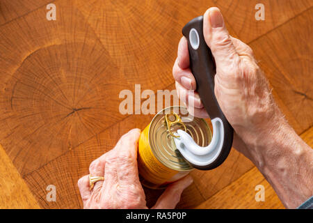 Man opening a tin can of canned food with a special opener on a wooden table while taking occupational therapy. Stock Photo