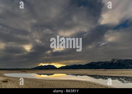 Cracked, dry soil with water surface and Allgäu Alps in the background, Forggensee, Füssen, Ostallgäu, Bavaria, Germany Stock Photo