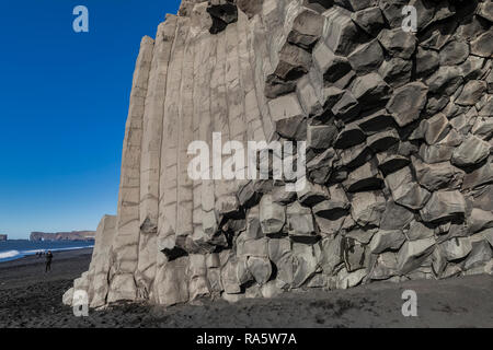 Columnar basalt formations along Reynisfjara Black Sand Beach, with Dyrholaey natural arch distant, in Iceland Stock Photo