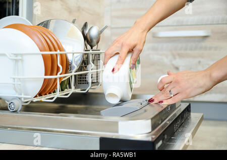 The woman's hand holding a bottle of detergent and adds it in the dishwasher. Stock Photo