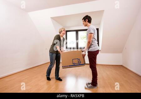 Young couple carrying the first moving box into the empty living room in a new apartment Stock Photo