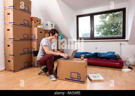 Young man sitting in an empty room in a new apartment, provisionally furnished with a sleeping bag, an air mattress Stock Photo
