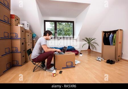 Young man sitting in an empty room in a new apartment, provisionally furnished with a sleeping bag, an air mattress Stock Photo