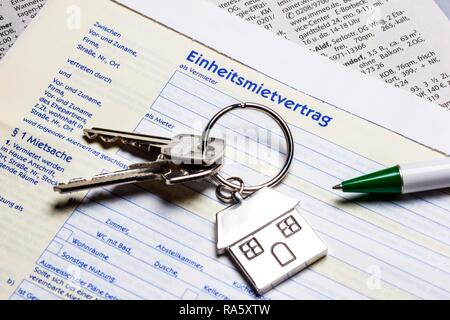 Two keys with a metal key tag shaped like a house lying on a German rental agreement, symbolic image for home, real estate Stock Photo
