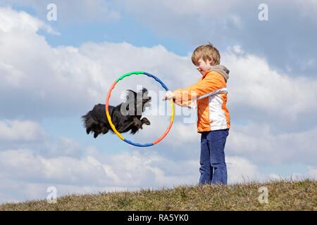 Dog jumping through a hoop held by a boy, Germany Stock Photo