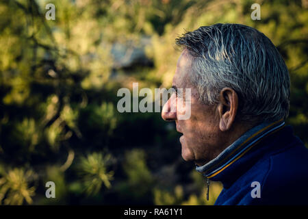 Attractive senior man with gray hair looking in foreground with vegetation background Stock Photo